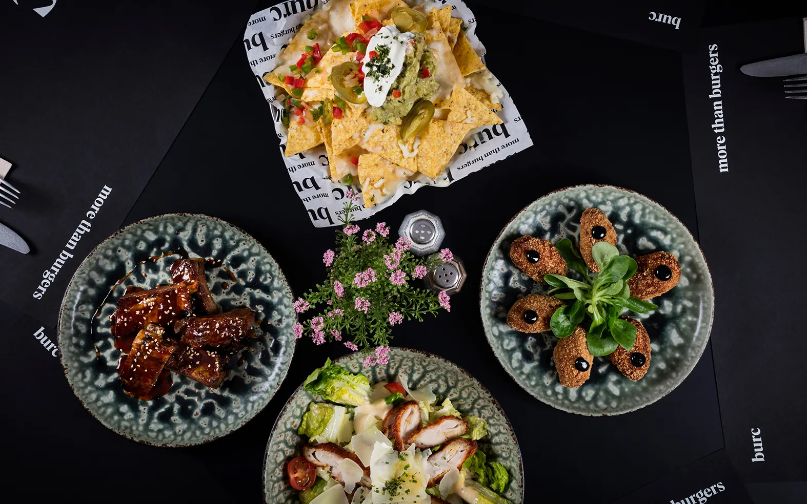 Vista cenital de varios entrantes: alitas, croquetas, nachos y ensalada sobre la mesa oscura